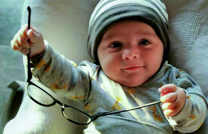 Lächelndes Baby spielt mit einer Brille und biegt dabei die Bügel auseinander.