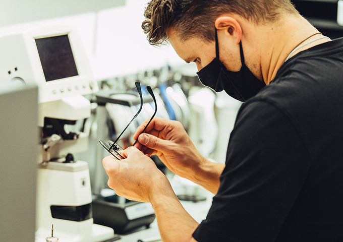 Augenoptiker mit Corona-Maske in der Werkstatt beim Ausrichten einer Brille.