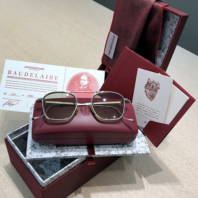 Sonnenbrille auf der Verpackungsbox von Jacques Marie Mage in bordeaus-rot mit Futter aus hellgrauem Marmorpapier mit Zertifikat und dem Sonnenbrillenmodell Baudelaire.
