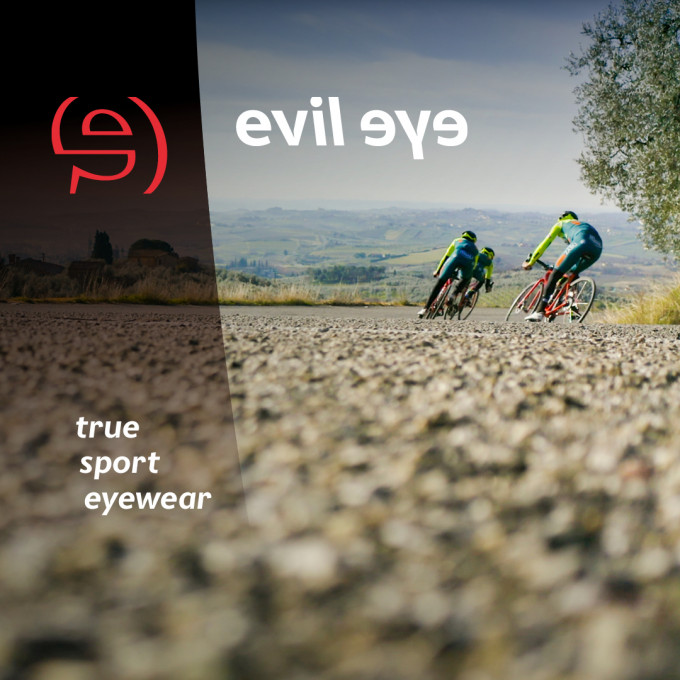 2 Rennradfahrer aus der Froschperspektive fahren um eine Kurve in einer hügeligen Landschaft.