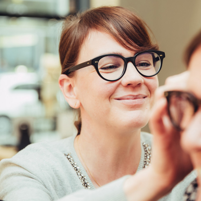 Lächelnde Augenoptikerin passt eine Brille an den Kopf ihrer Kundin an.