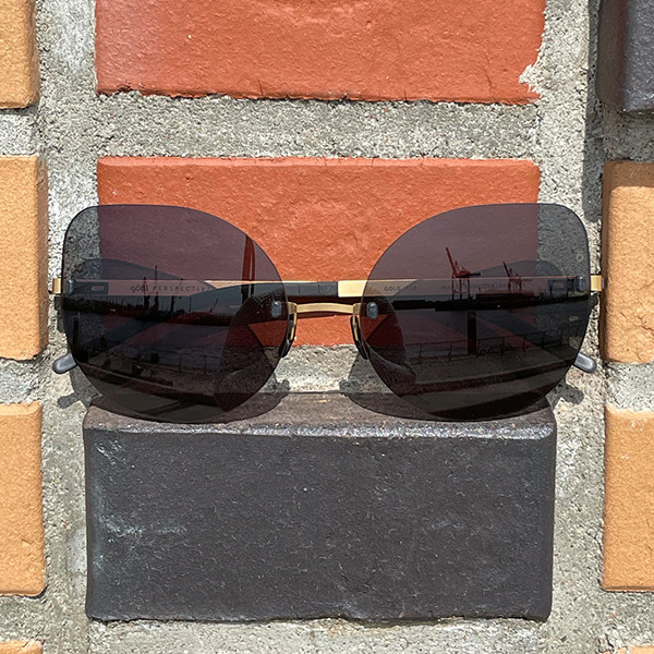 Randlose Brille mit goldener Garnitur und Schmetterlingsform vor einer Ziegelwand.