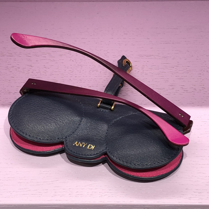 Dunkelblaues Nappaleder Brillenetui von AnyDi mit Futter in pink und einer Brille mit pinken Brillenbügeln.