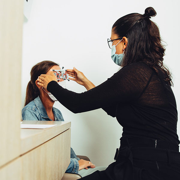 Augenoptikerin setzt einer Kundin die Prüfbrille für den Sehtest auf.