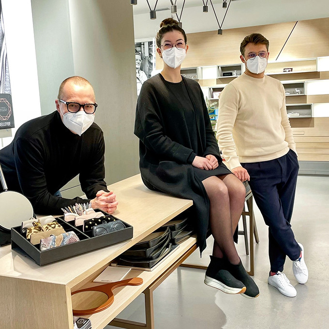 2 Optiker und eine Optikerin aus dem BELLEVUE Team stehen und sitzen am mittleren Beratungstisch und erwarten neue Kunden.