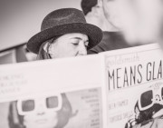 Claire Goldsmith mit Hut, halb verdeckt von einer Zeitung mit Fotos ihrer Oliver Goldsmith Kollektion.