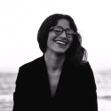 Ahlem Manai-Platt mit einer Kunststoffbrille aus ihrer Kollektion Ahlem vor einer weiten unscharfen Naturlandschaft.