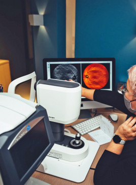 Augenoptikerin von BELLEVUE mit Kundin an einem Gerät zum Netzhaut-Scan. Die Optikerin erklärt das Abbild der Netzhaut auf dem Bildschirm.