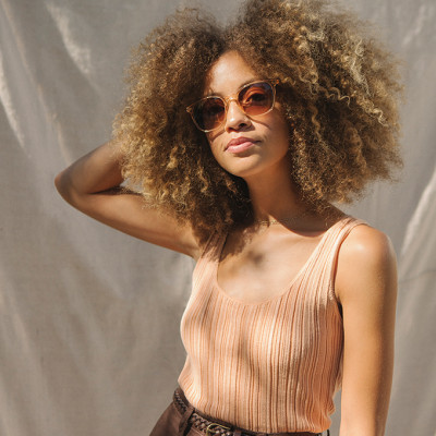 Frauenportrait mit hellbrauner Sonnenbrille und braunen Locken im Afro-Look