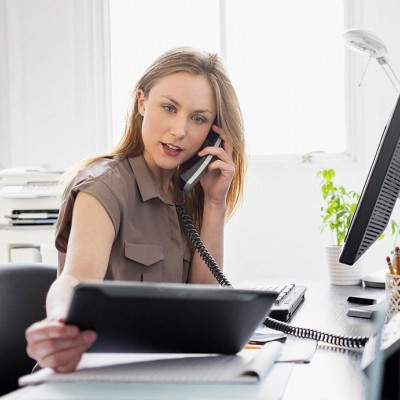 Junge Frau im Büro, gleichzeitig mit Bildschirm, Tablett und Telefon hantierend.